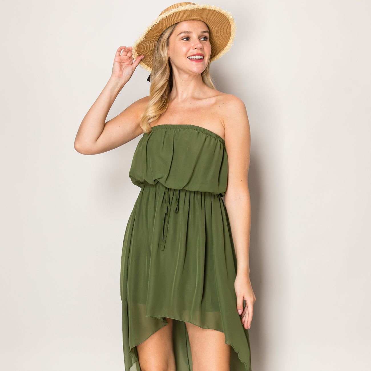 A cheerful woman wearing a green dress and straw hat posing indoors.
