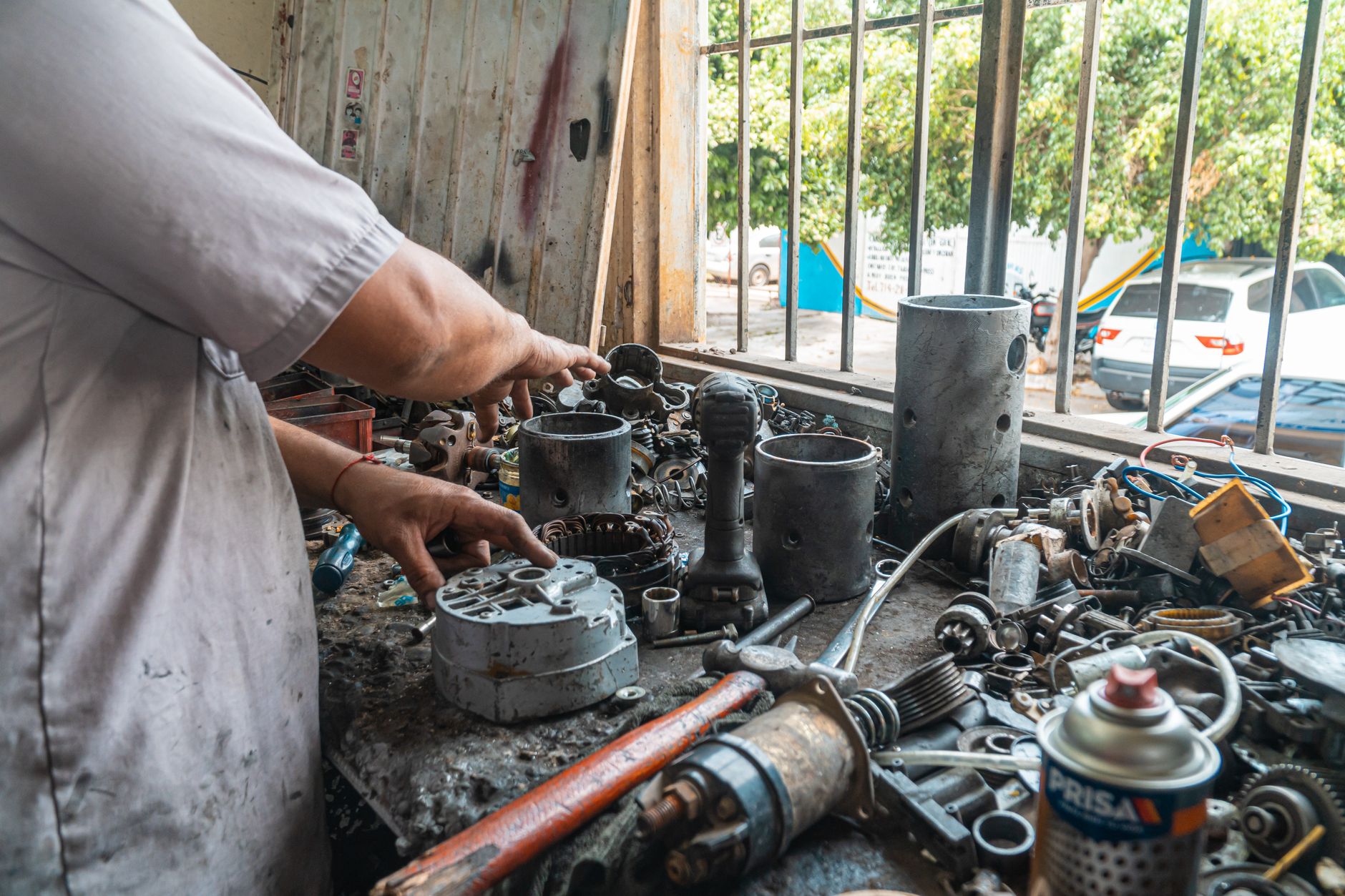 Mechanic arranging car parts on a cluttered work table in an automotive workshop.