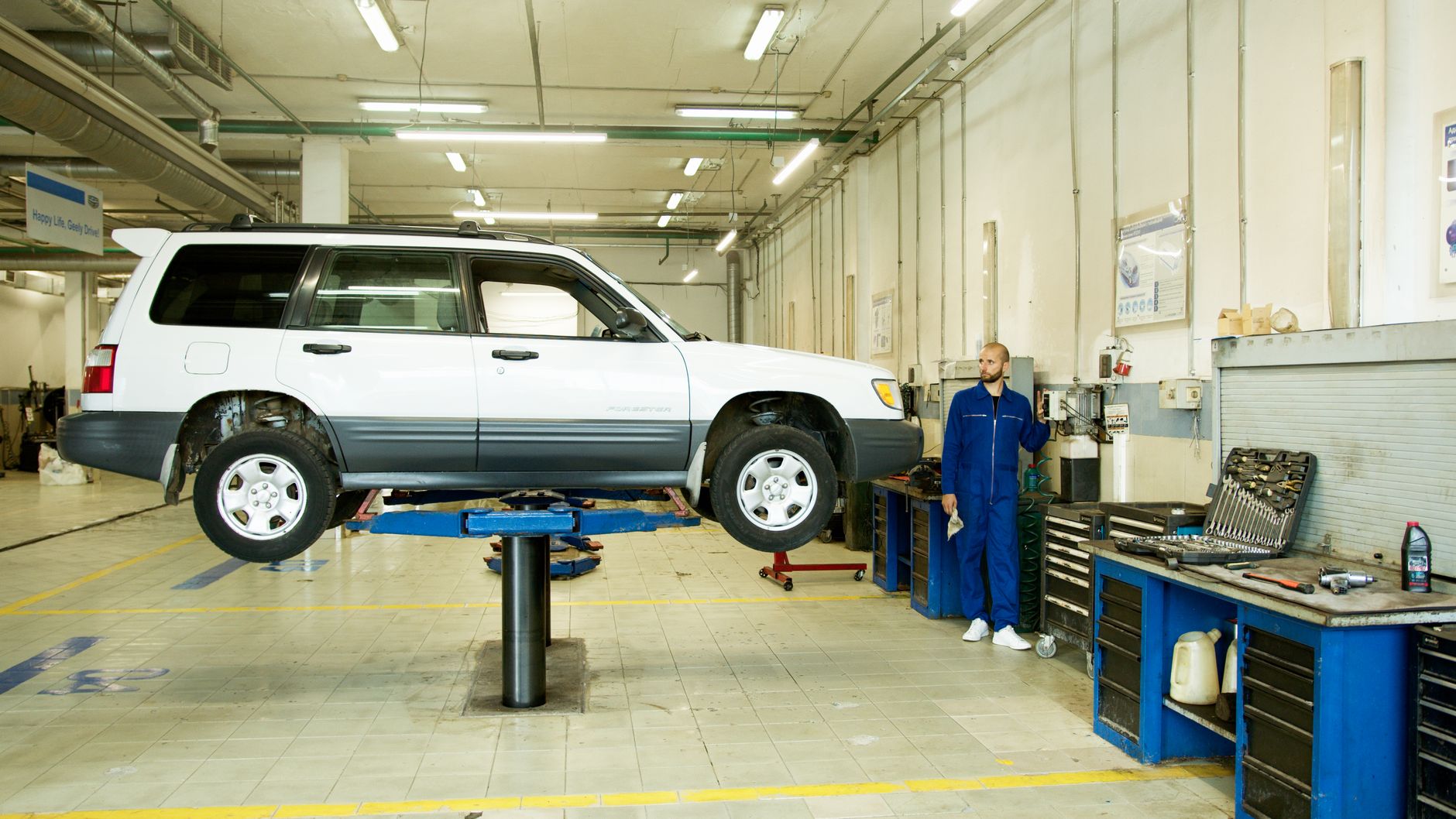 Mechanic in blue coveralls working on a vehicle lift in a well-equipped garage.