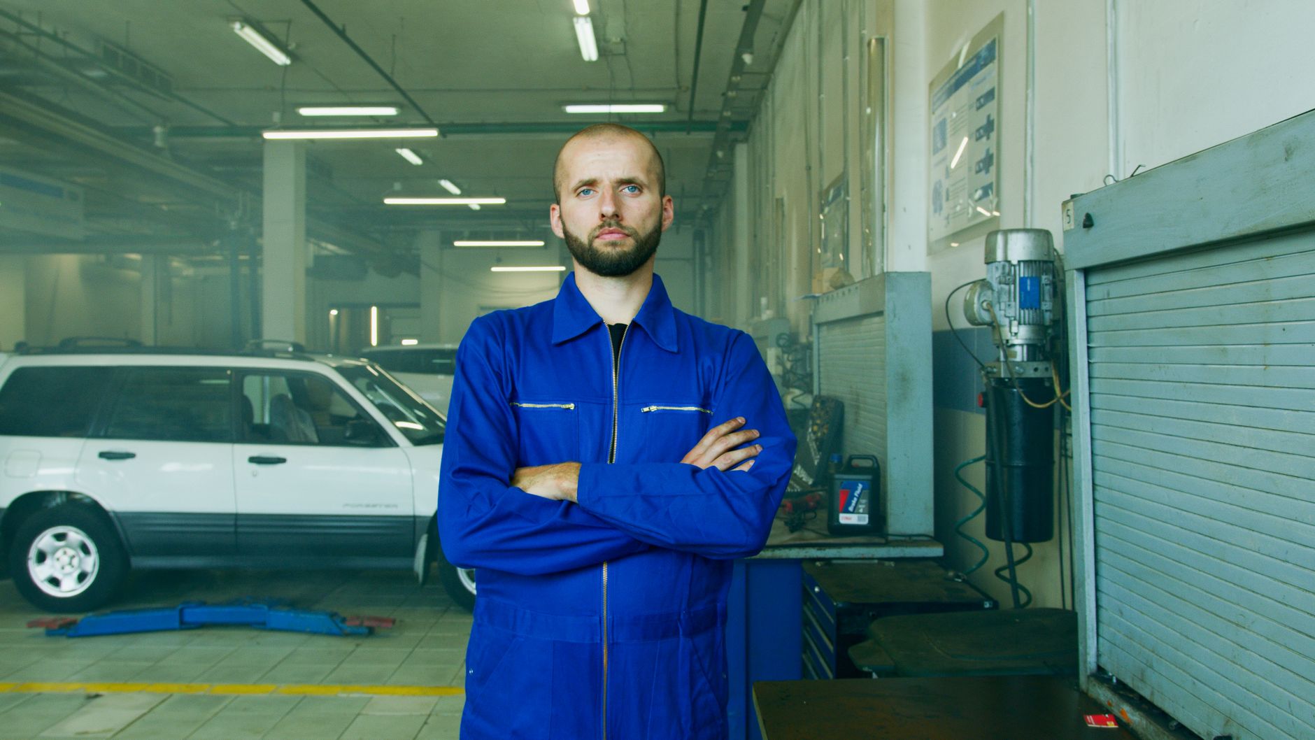 Technician in a blue boiler suit standing beside a white car in the workshop