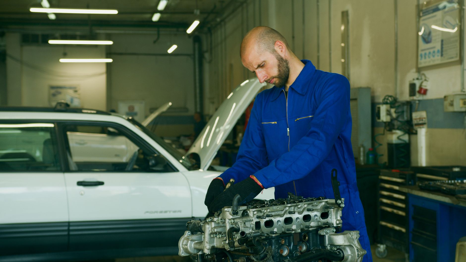Mechanic in a blue coverall inspecting a car engine in a garage workshop