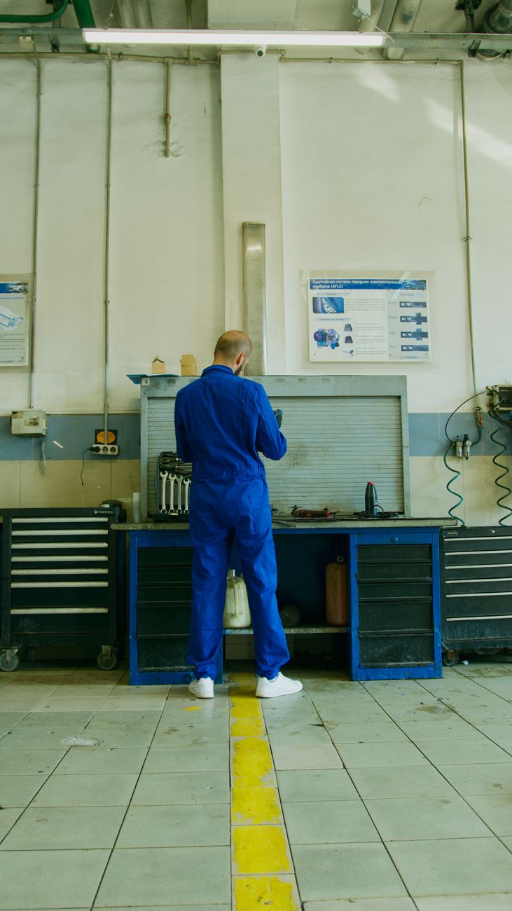 Mechanic in a blue coverall performing maintenance in a well-equipped workshop