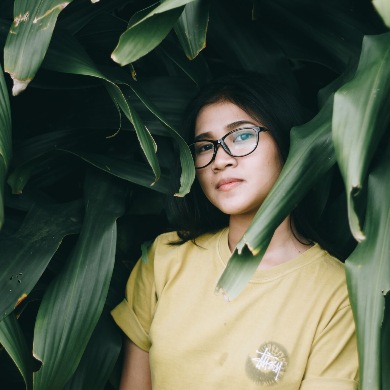 A young woman wearing glasses among green leaves
