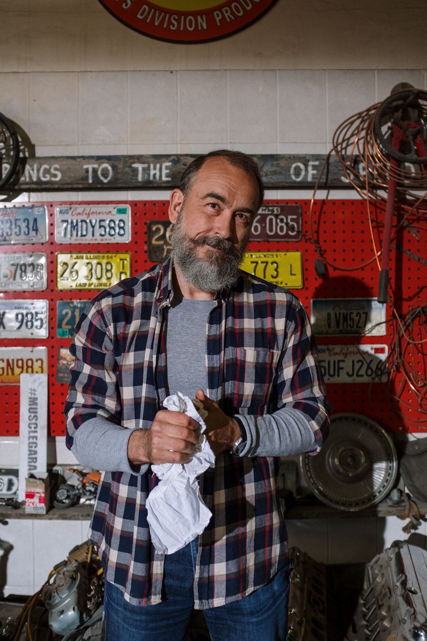 Photo of the shop owner standing in the garage among license plates and car parts