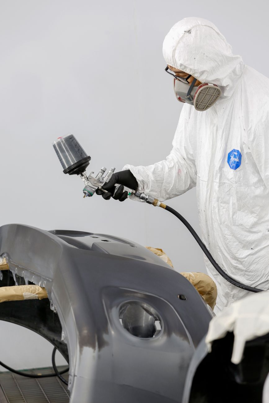 A technician in protective gear spray painting a car bumper