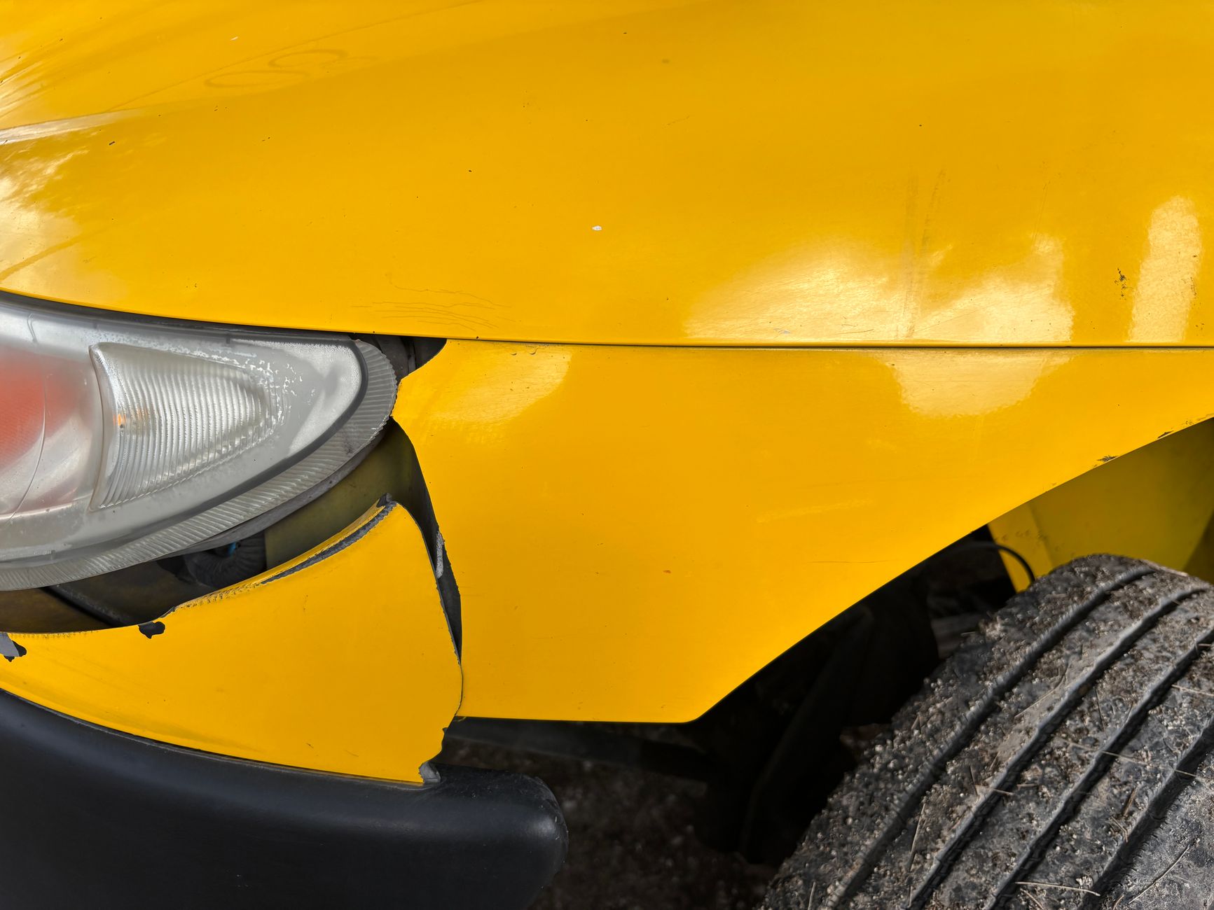 A yellow car with a damaged front bumper and headlight