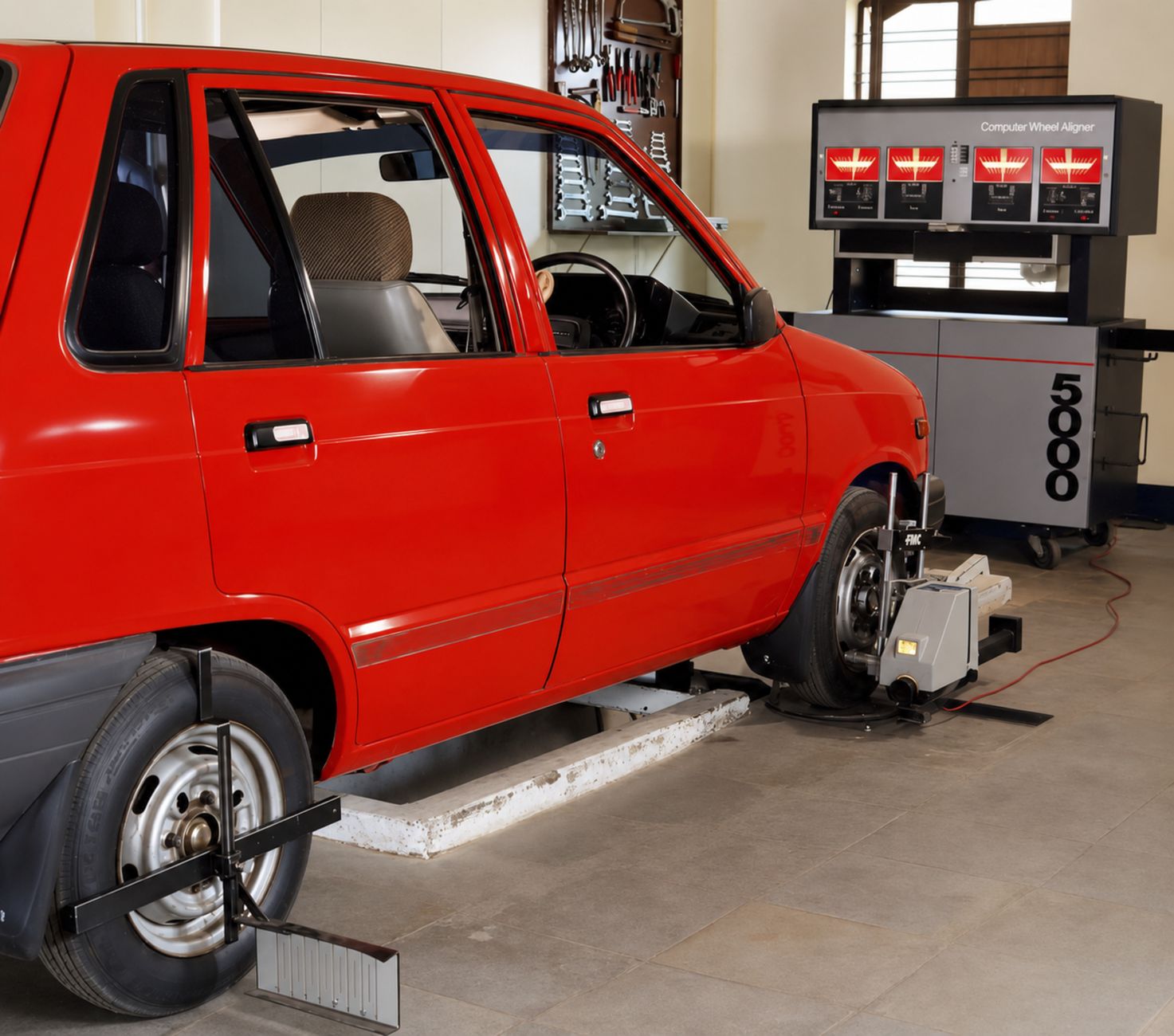 A red compact car on a computerised wheel alignment machine