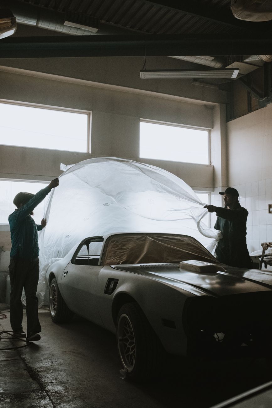 Mechanics working on a classic car restoration in a well-lit garage