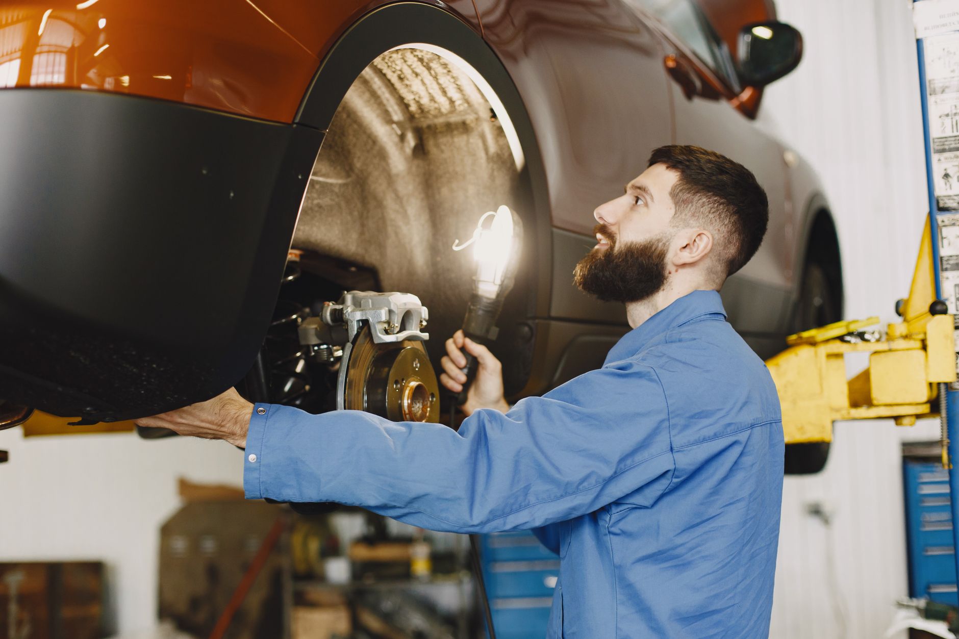 A mechanic in coveralls inspecting the brakes of a lifted car