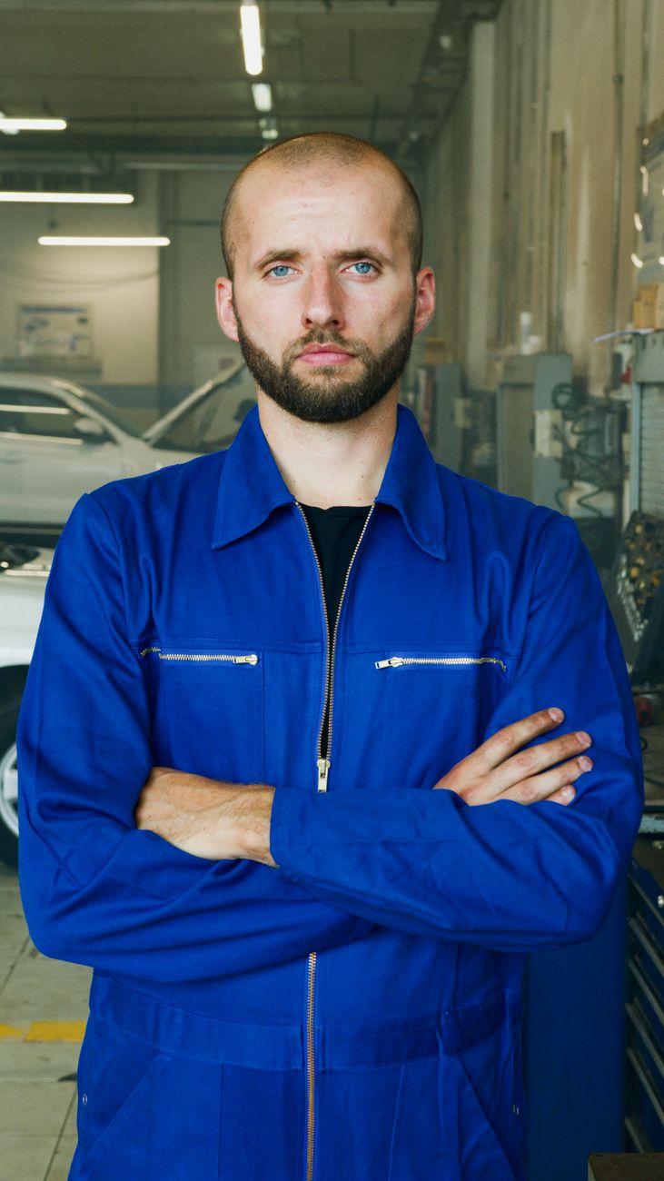 A mechanic in a blue uniform standing with arms crossed in the garage