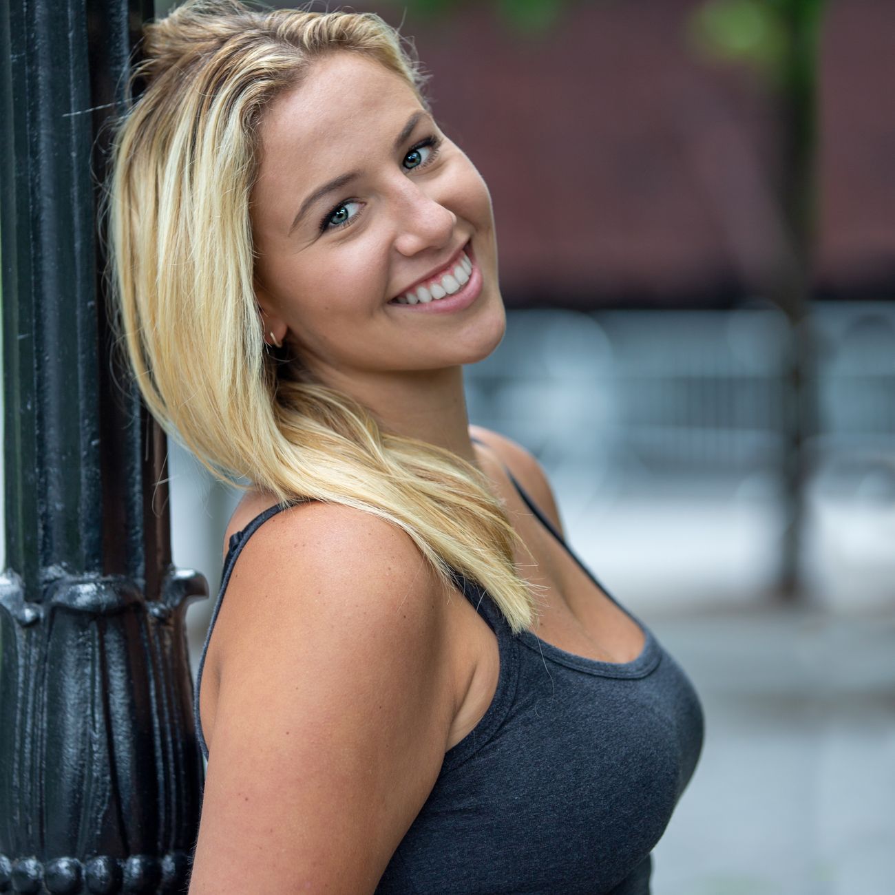 A smiling woman leaning against a lamp post outdoors