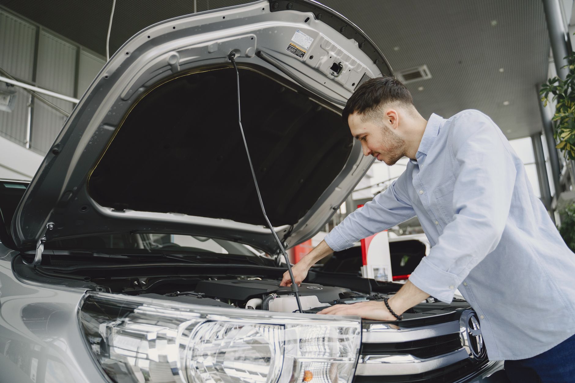 A man in a blue shirt examining a car's engine in a showroom