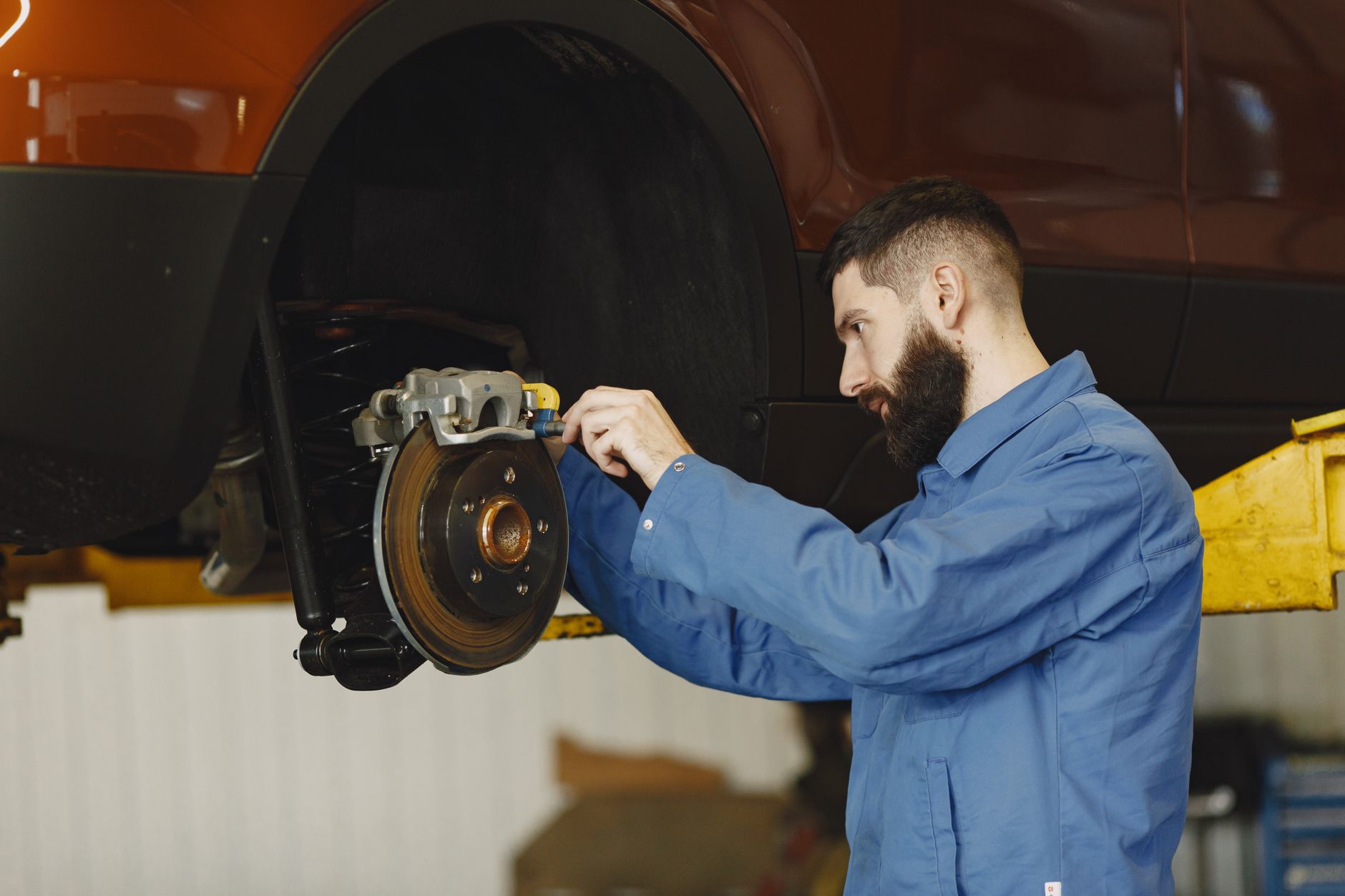 A mechanic in a blue uniform repairing a car brake in a garage