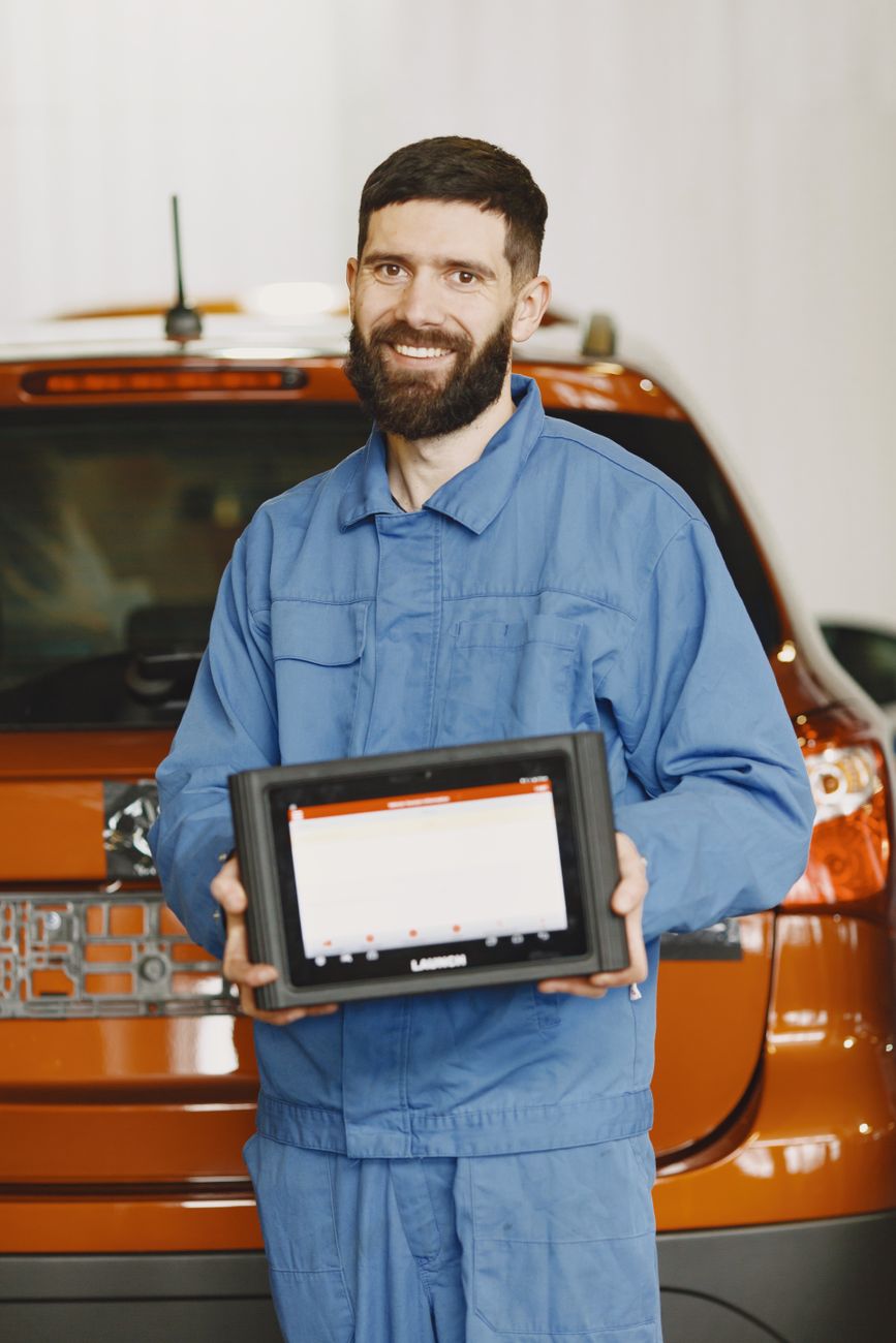 An auto mechanic in blue coveralls holding a diagnostic tablet