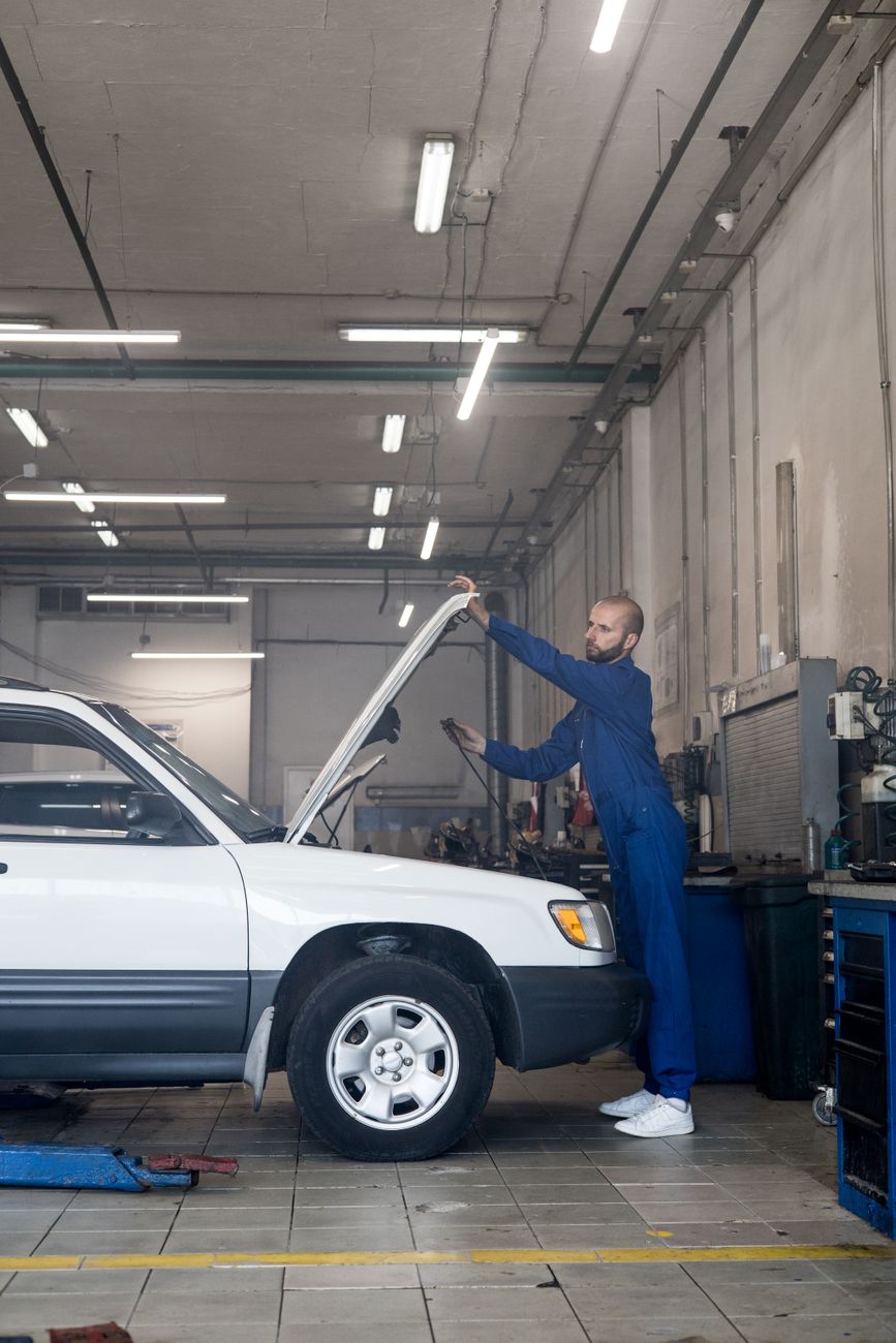 A mechanic checking under the hood of a car in a repair shop