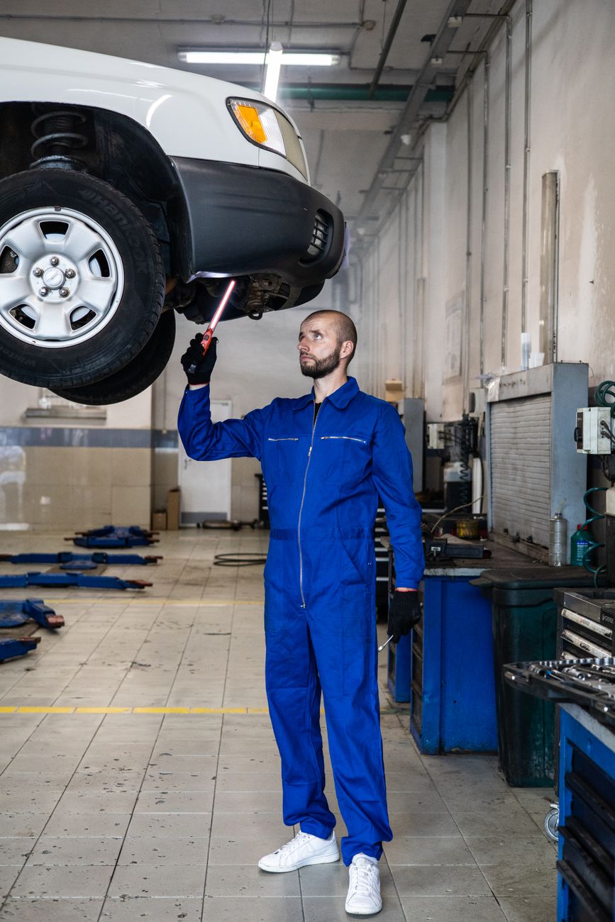 A mechanic in blue coveralls inspecting a car in a repair shop