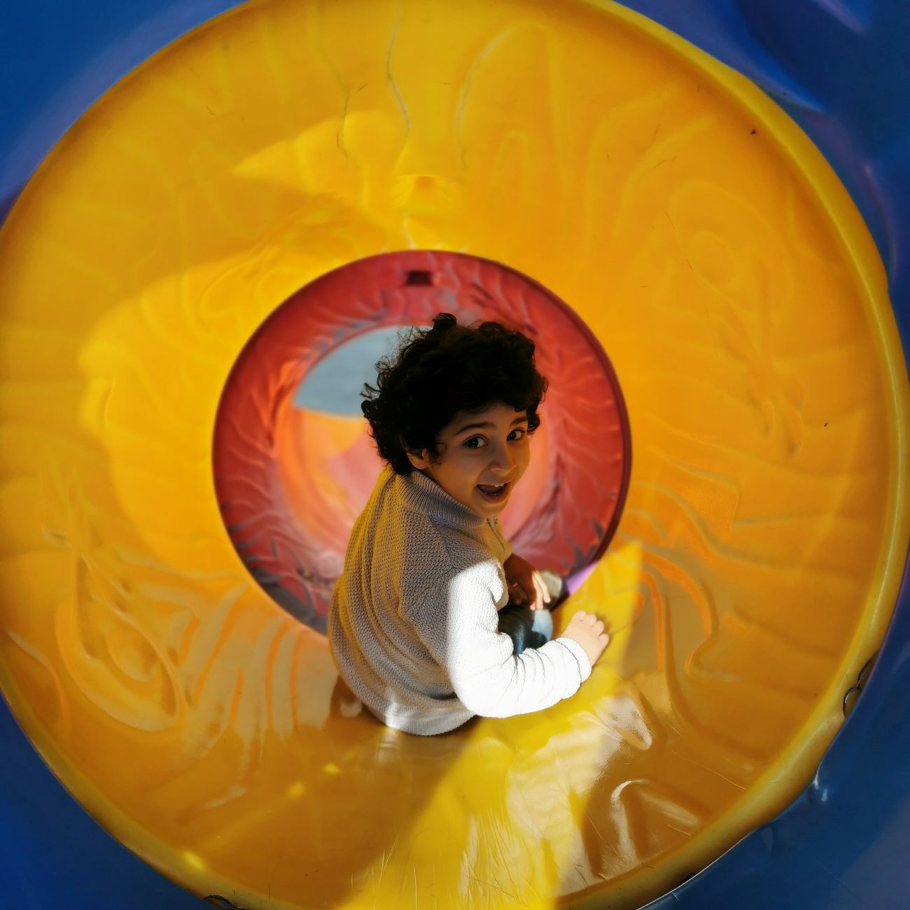 A child sliding through a bright playground tunnel