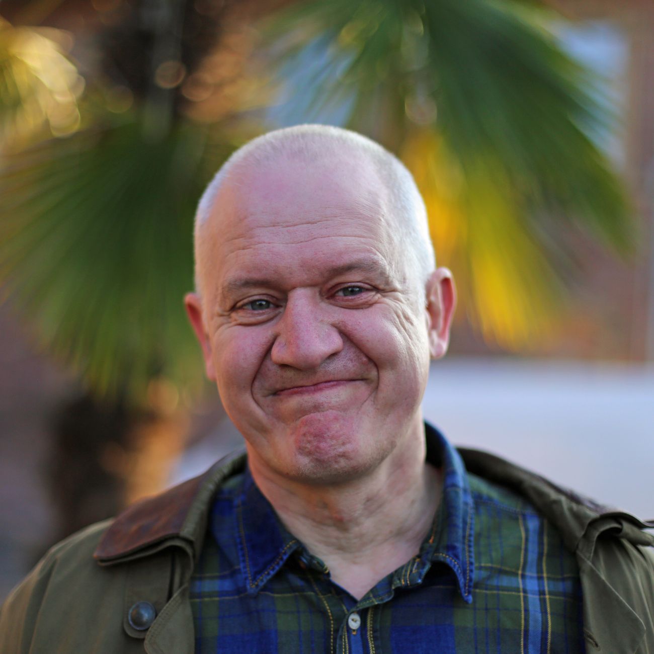 A smiling bald man outdoors with a palm tree behind him