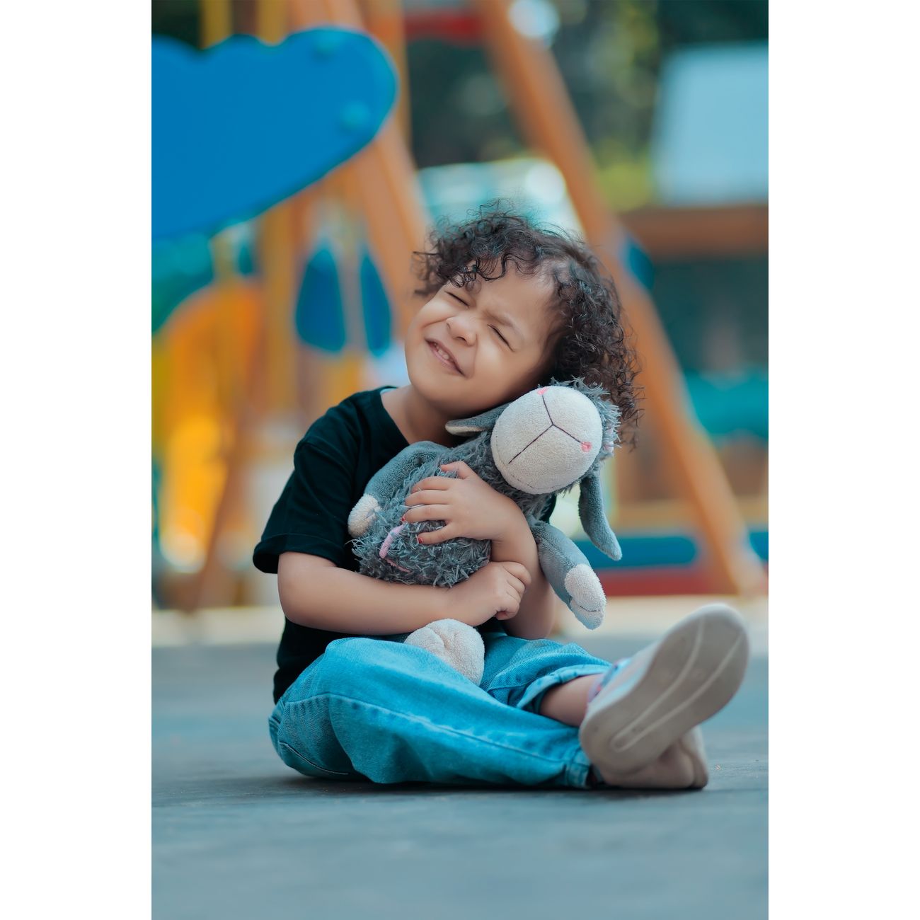 A smiling child with curly hair hugging a plush toy on a playground