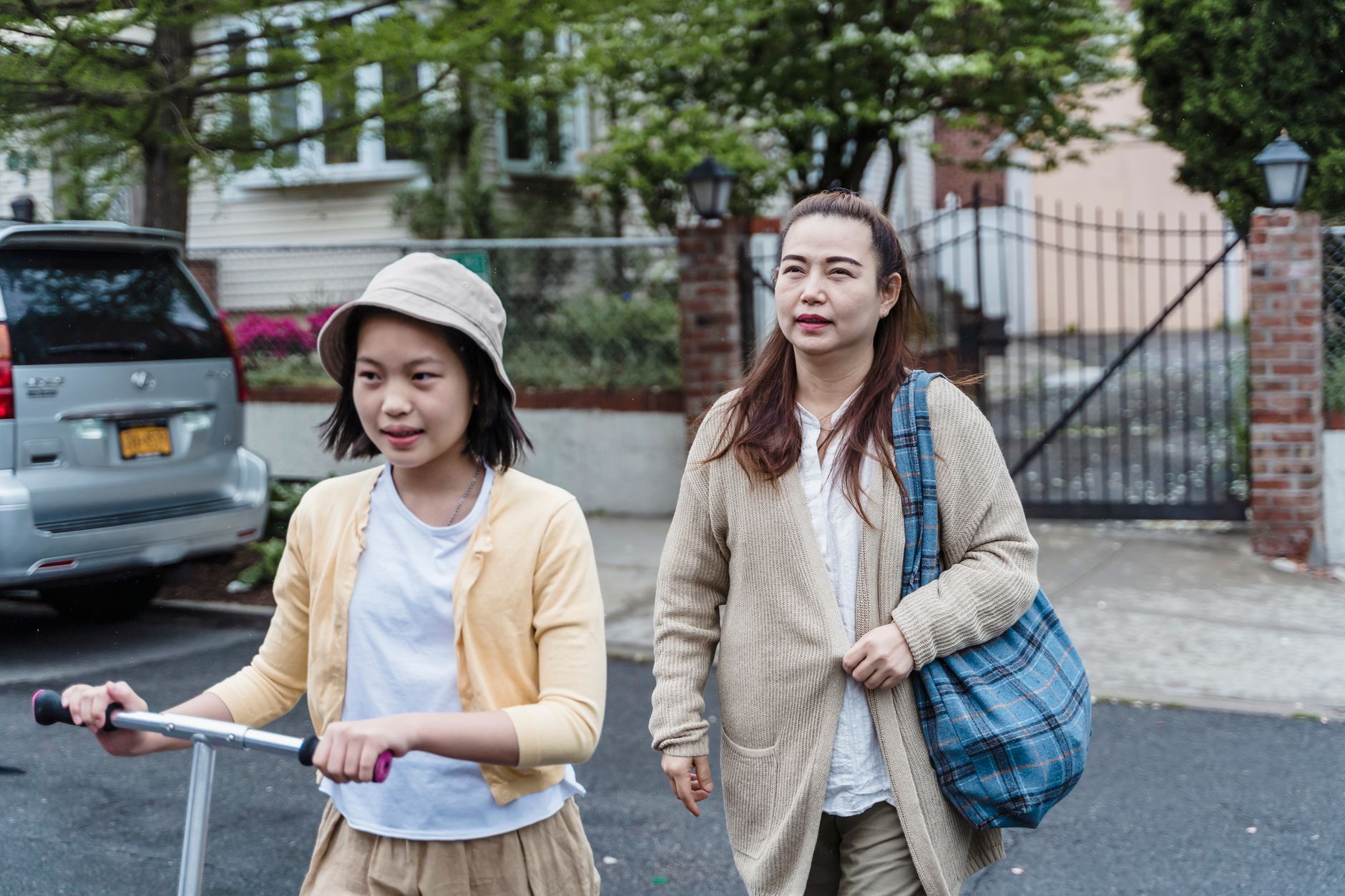 A mother and her daughter walking with a scooter in a neighbourhood