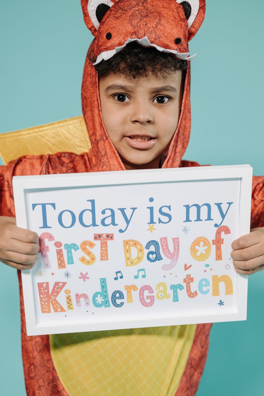 Child in dragon costume holding a sign for first day of kindergarten.
