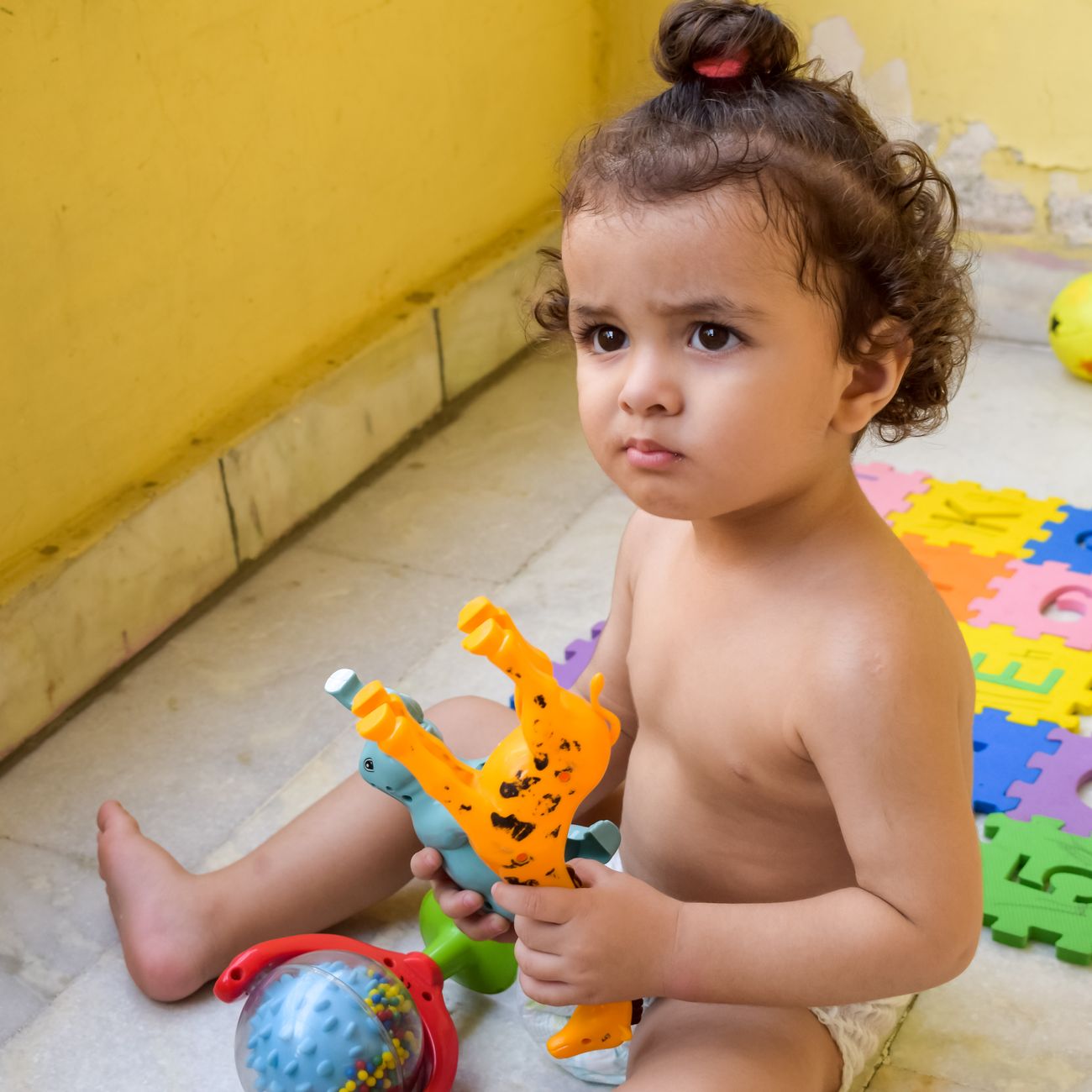 Cute toddler focused on playing with colorful plastic toys indoors on a sunny day.