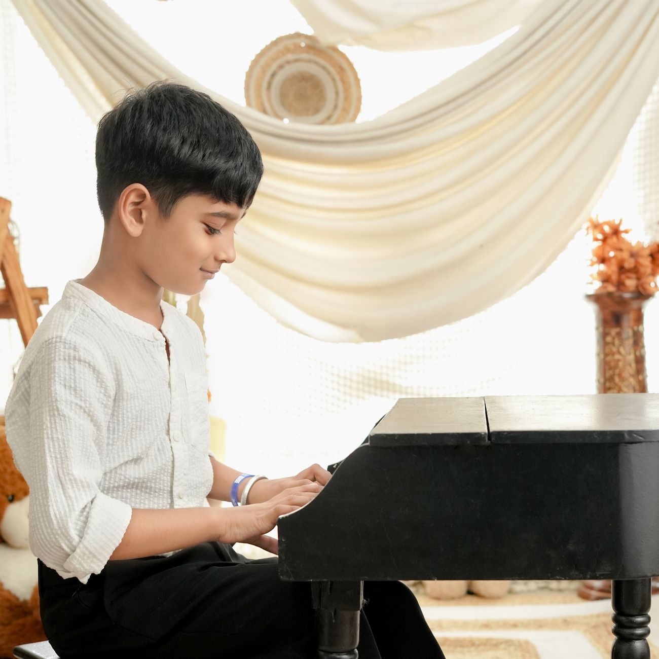 A young boy enthusiastically playing the piano in a bright, decorated room.