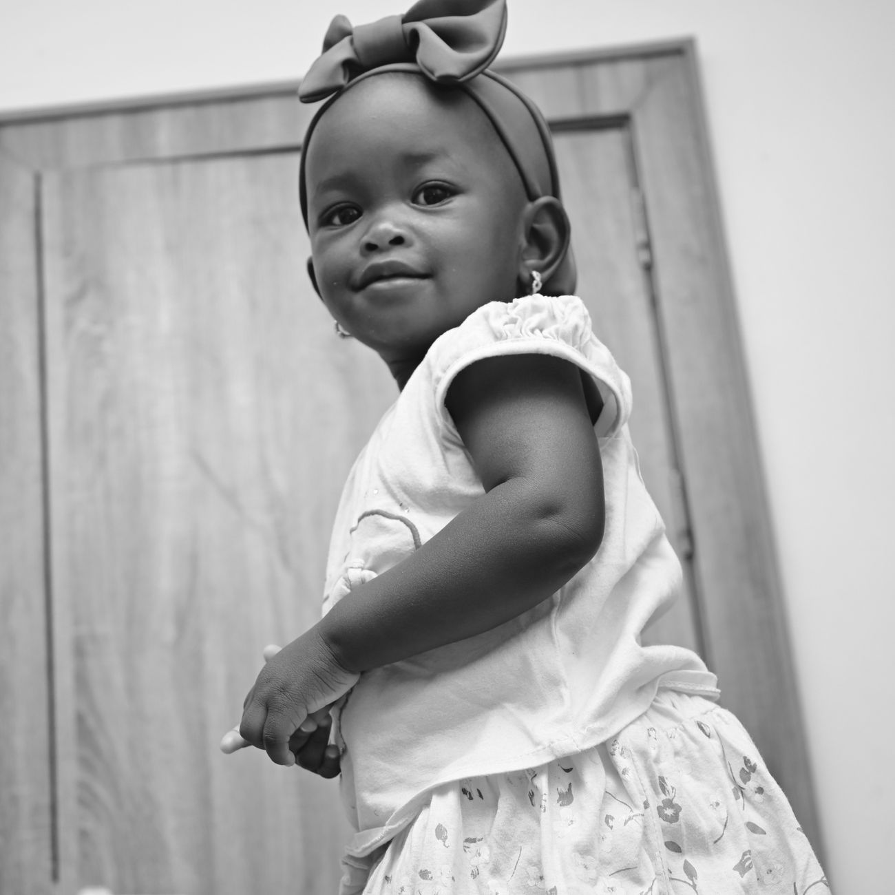 Charming black and white portrait of a happy toddler girl indoors wearing a bow headband.
